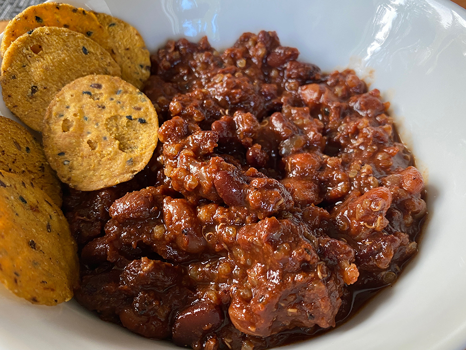 Bowl of rich and thick chili with sweet potato crackers on the side
