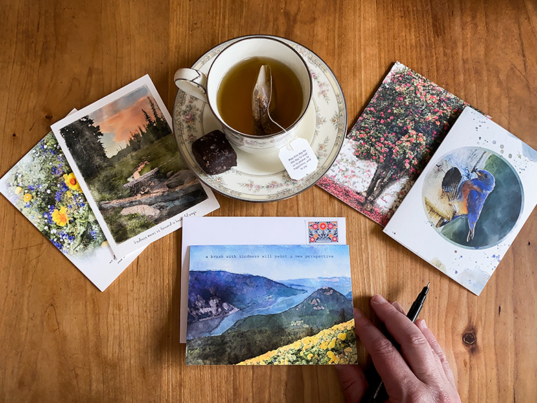 Flat-lay photo of 5 gratitude cards, a stamped envelop, and cup of tea with a salted chocolate