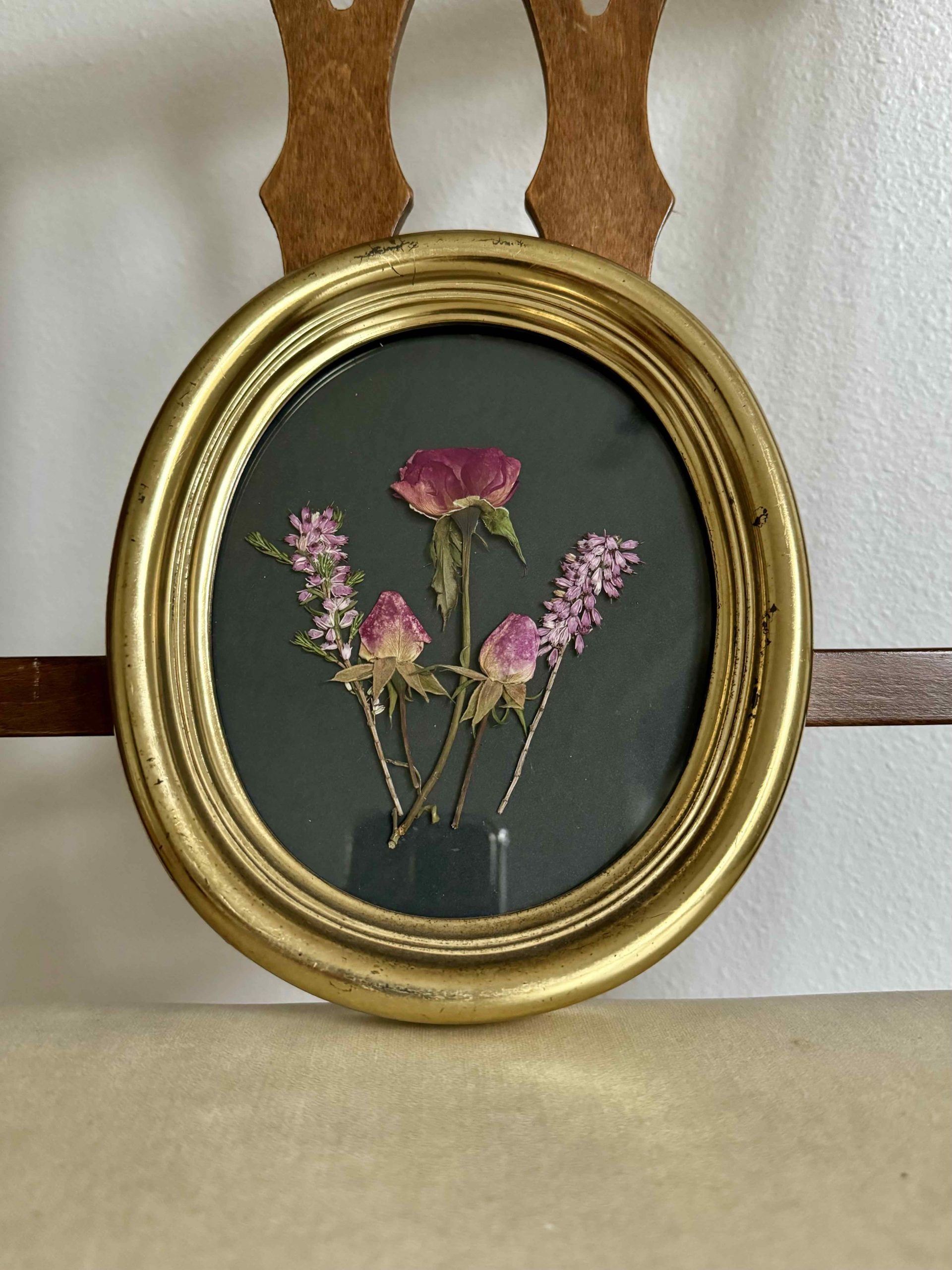 Three pink rose buds and two heather blooms pressed on black paper in oval vintage frame by Kindness Roots